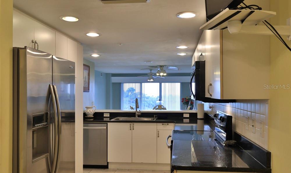 A kitchen with stainless steel appliances, white cabinets, and black countertops overlooks a living area — 4 OCEANS WEST BOULEVARD UNIT 508D, DAYTONA BEACH SHORES, FL