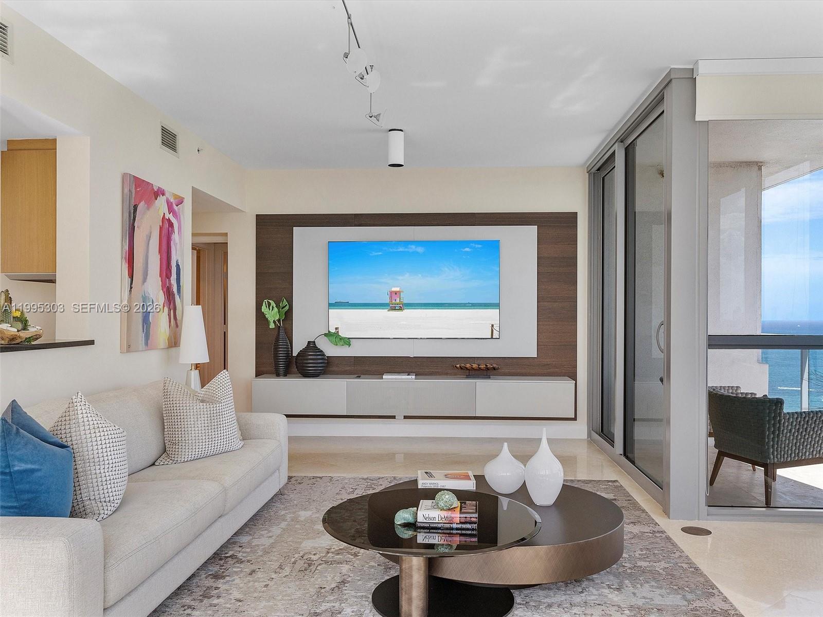 A modern living room features a wall-mounted television, a neutral sofa, and a glass balcony — 101 20th St # 3002, Miami Beach FL 33139, MIAMI BEACH, FL