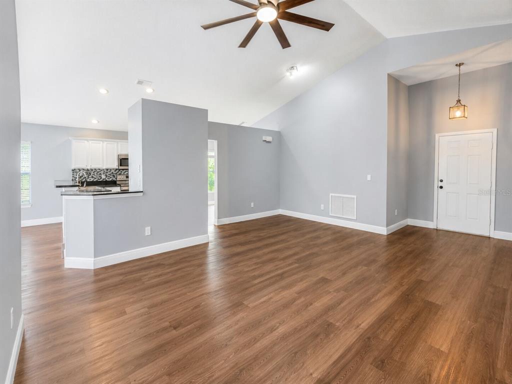 An open-concept living area with light gray walls, wood-look flooring, and a kitchen peninsula — 1926 DARLIN CIRCLE, ORLANDO, FL