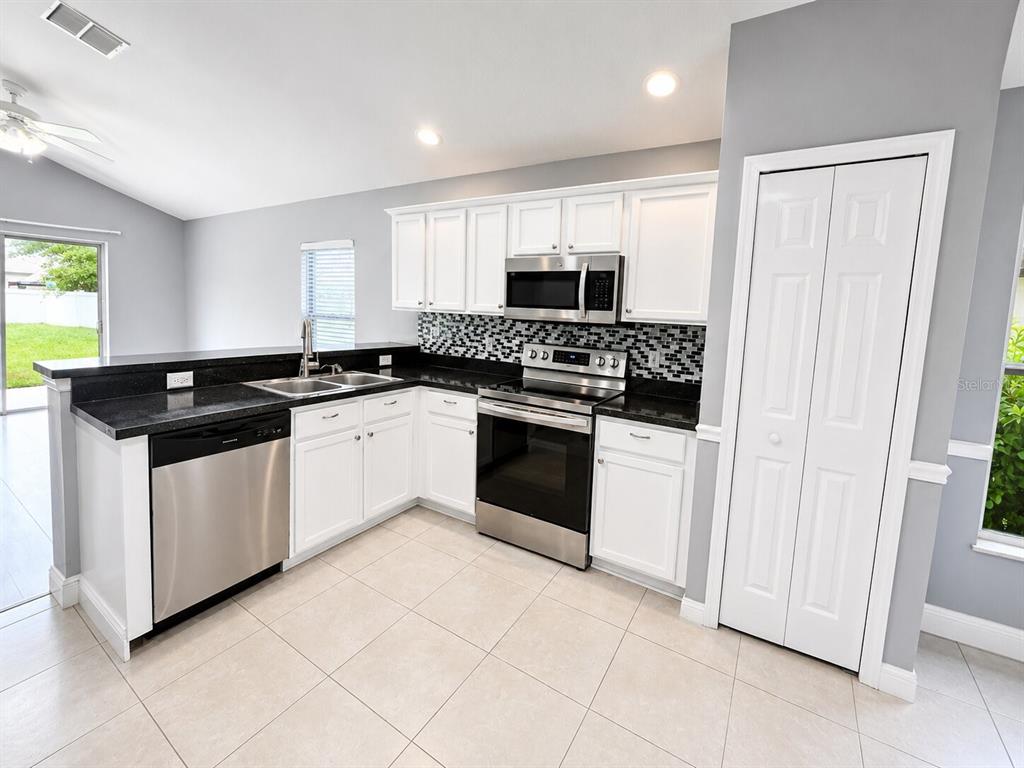 A kitchen features white cabinets, black countertops, stainless steel appliances, and light-colored floor tiles — 1926 DARLIN CIRCLE, ORLANDO, FL