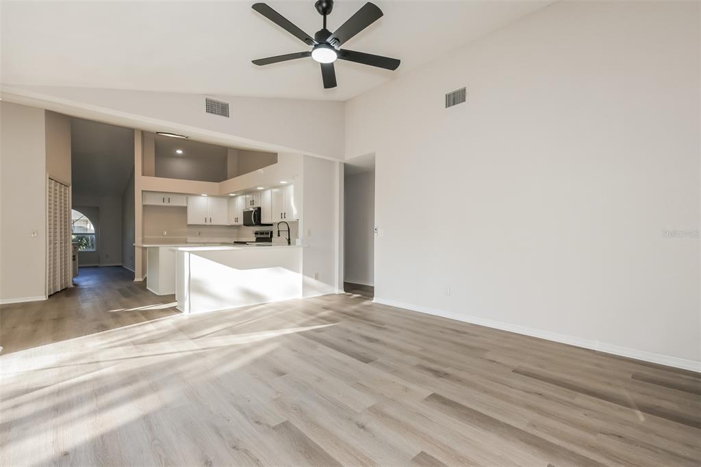 A living room with light wood-look flooring, a vaulted ceiling, and an open kitchen — 2624 BRIDLE DRIVE, PLANT CITY, FL