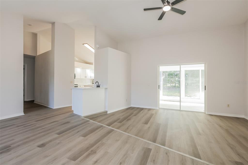An open-concept living area features light wood-look flooring, a kitchen peninsula, and sliding glass doors — 2624 BRIDLE DRIVE, PLANT CITY, FL