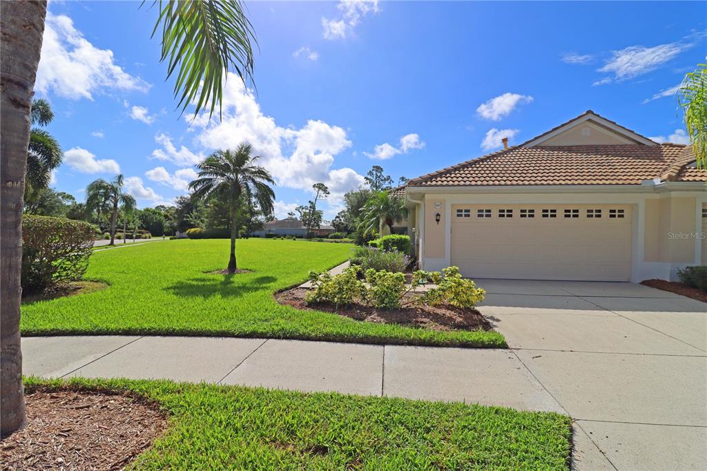 A single-story house with a beige garage and a large green lawn under blue skies — 5107 WHISPERING OAKS DRIVE, NORTH PORT, FL