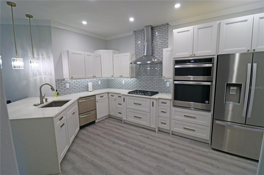 A modern kitchen features white cabinets, stainless steel appliances, a gray tile backsplash, and wood-look flooring — 5107 WHISPERING OAKS DRIVE, NORTH PORT, FL