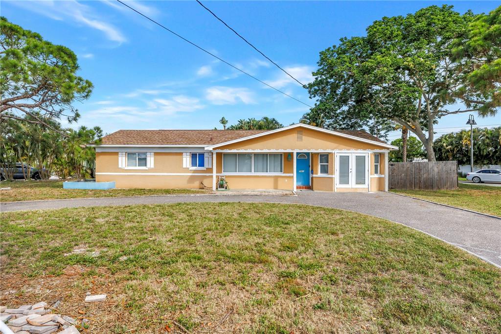 A single-story house with a tan exterior, a blue front door, and a curved driveway — 7901 CAUSEWAY BOULEVARD S, ST PETERSBURG, FL