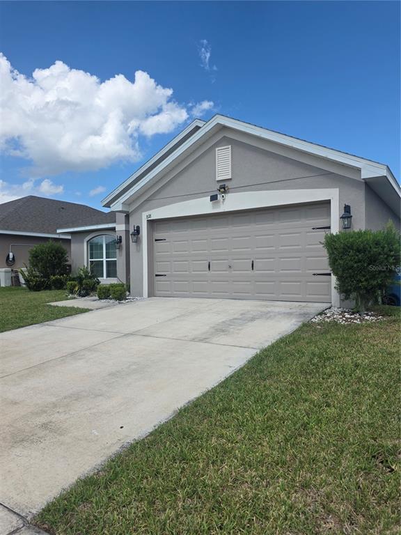A beige single-story house features a two-car garage, a concrete driveway, and a grassy lawn — 818 LANDMARK HILLS DRIVE, HAINES CITY, FL