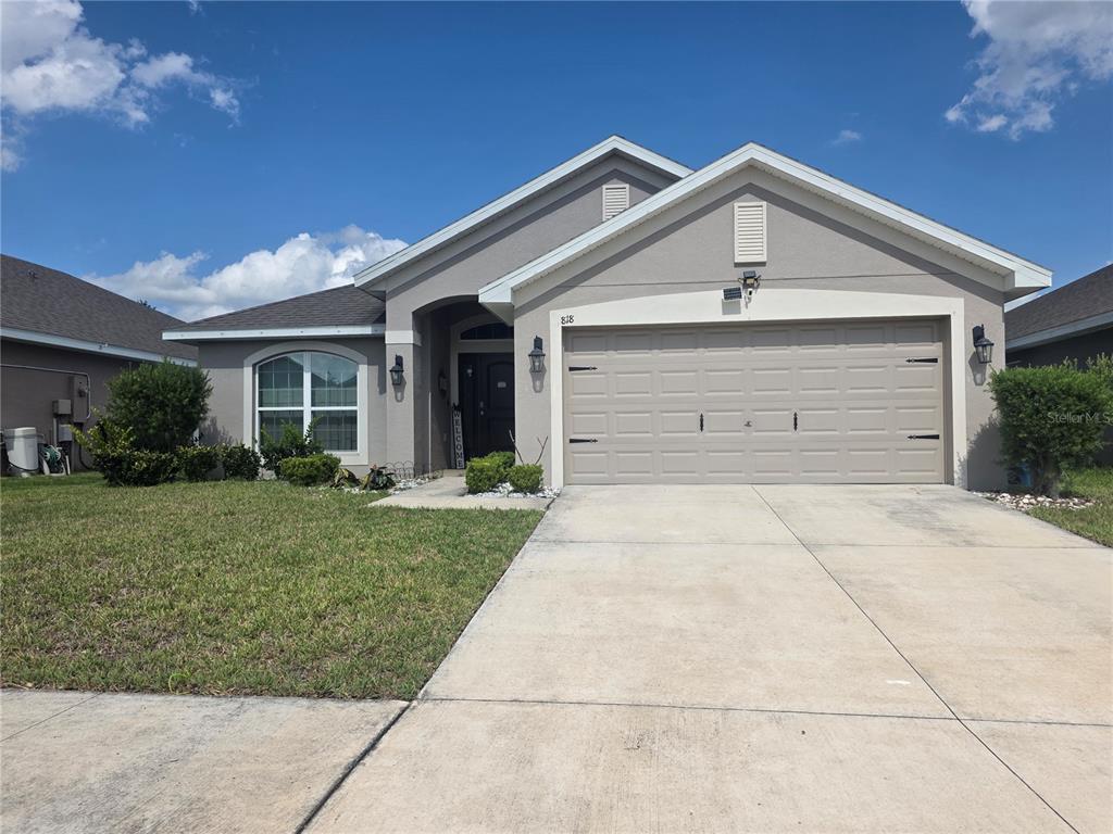 A single-story house with a gray stucco exterior, a two-car garage, and a front lawn — 818 LANDMARK HILLS DRIVE, HAINES CITY, FL