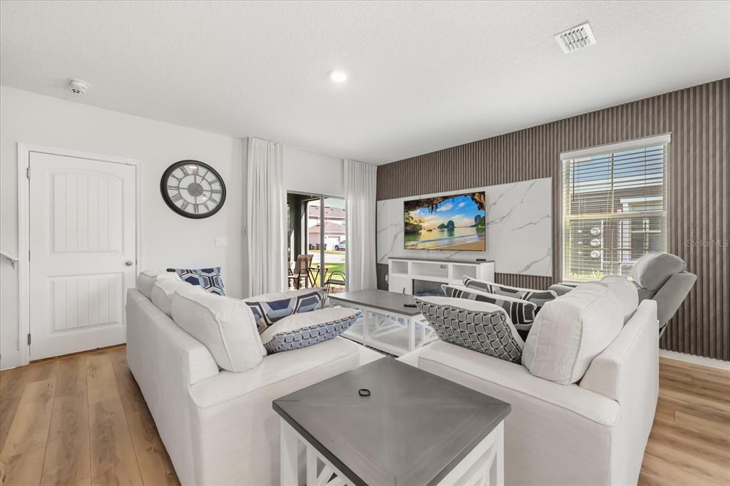 A living room features white sofas, a television on a marble-accented wall, and wood flooring — 10089 SALT POINT DRIVE, WINTER GARDEN, FL