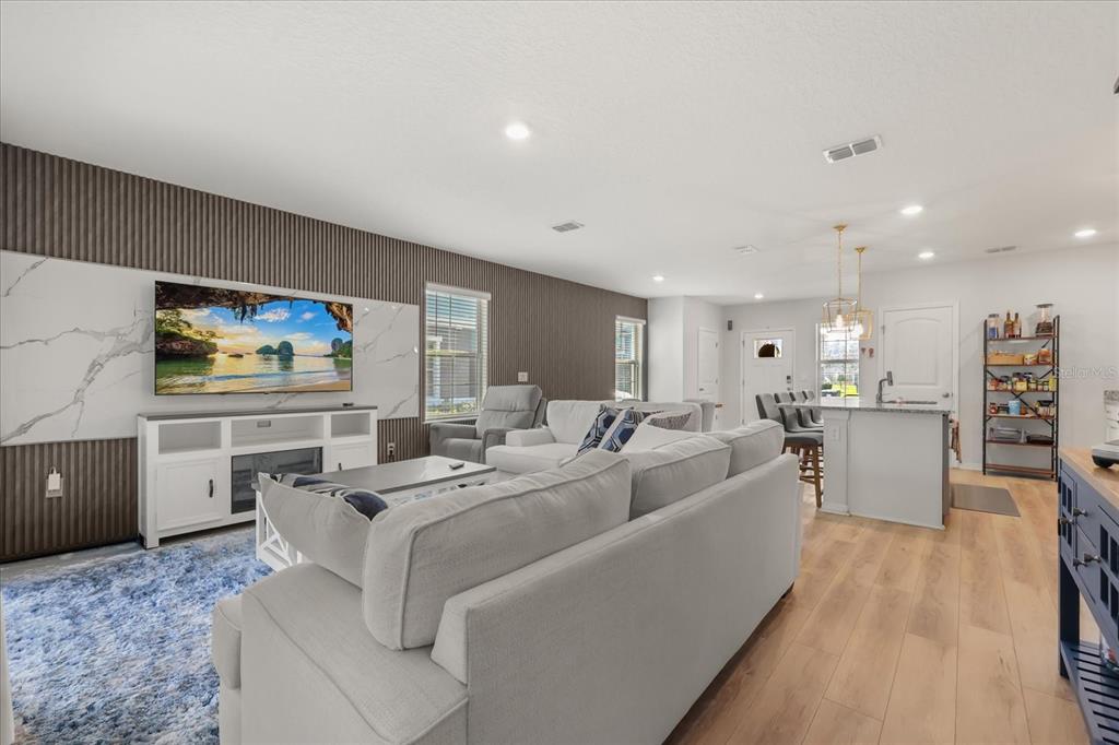 A living room features a marble-accented media wall, a white sofa, and light wood flooring — 10089 SALT POINT DRIVE, WINTER GARDEN, FL