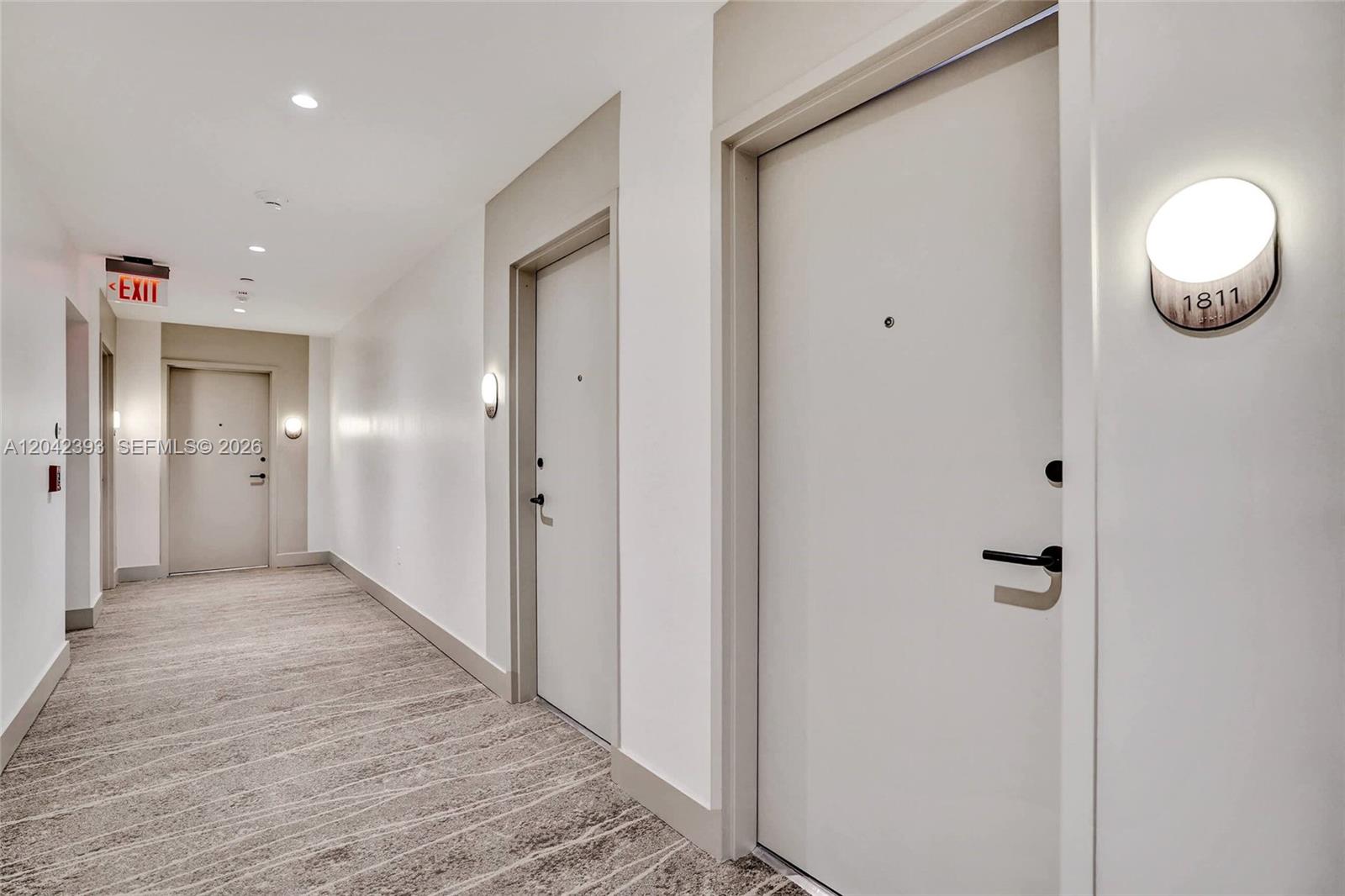 A brightly lit apartment hallway features carpeted floors, white walls, and several numbered unit doors — 580 72nd St # 1811, Miami Beach FL 33141, MIAMI BEACH, FL