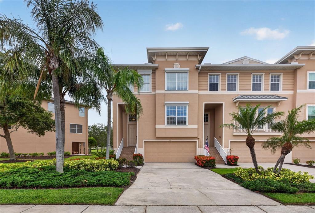 A three-story tan townhouse with a two-car garage, palm trees, and a concrete driveway — 7172 ISLAMORADA CIRCLE, SEMINOLE, FL