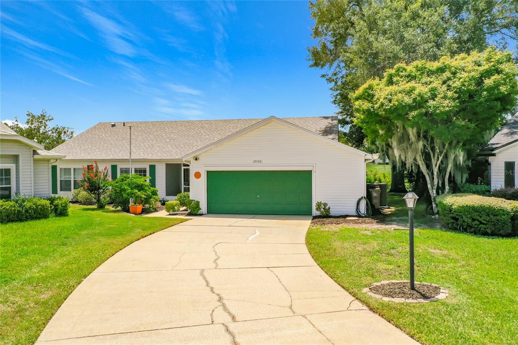 A single-story house with white siding, a green garage door, and a cracked concrete driveway — 25106 MERIWEATHER ROAD, LEESBURG, FL