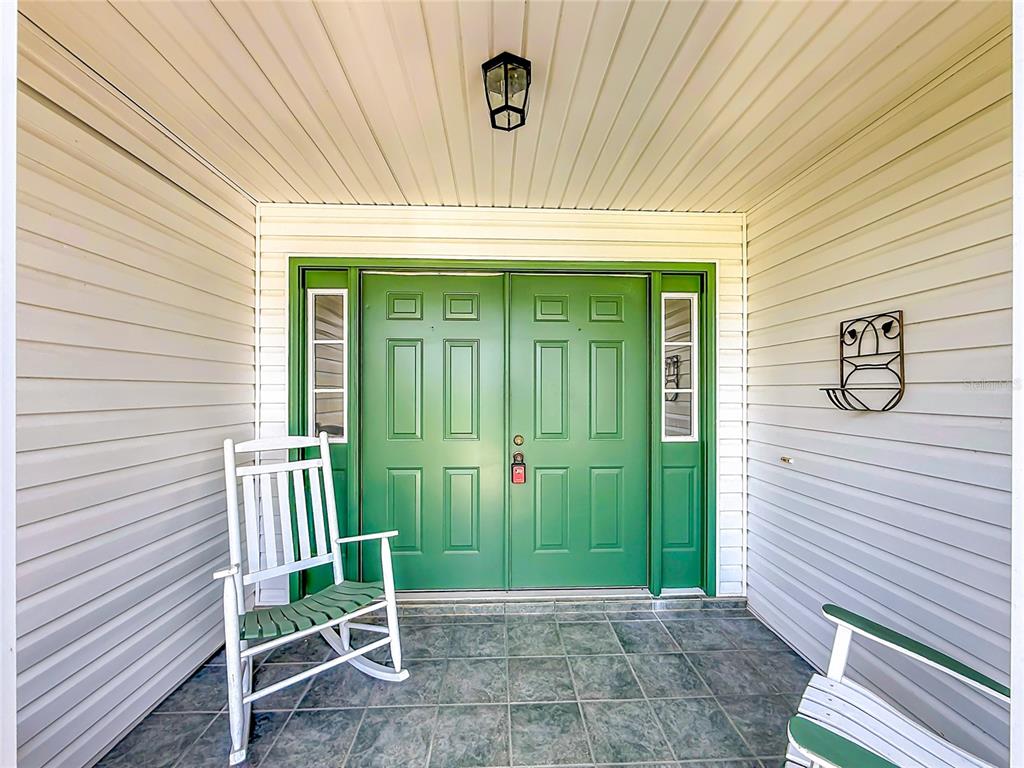 A covered front porch features green double doors, white siding, and two wooden rocking chairs — 25106 MERIWEATHER ROAD, LEESBURG, FL