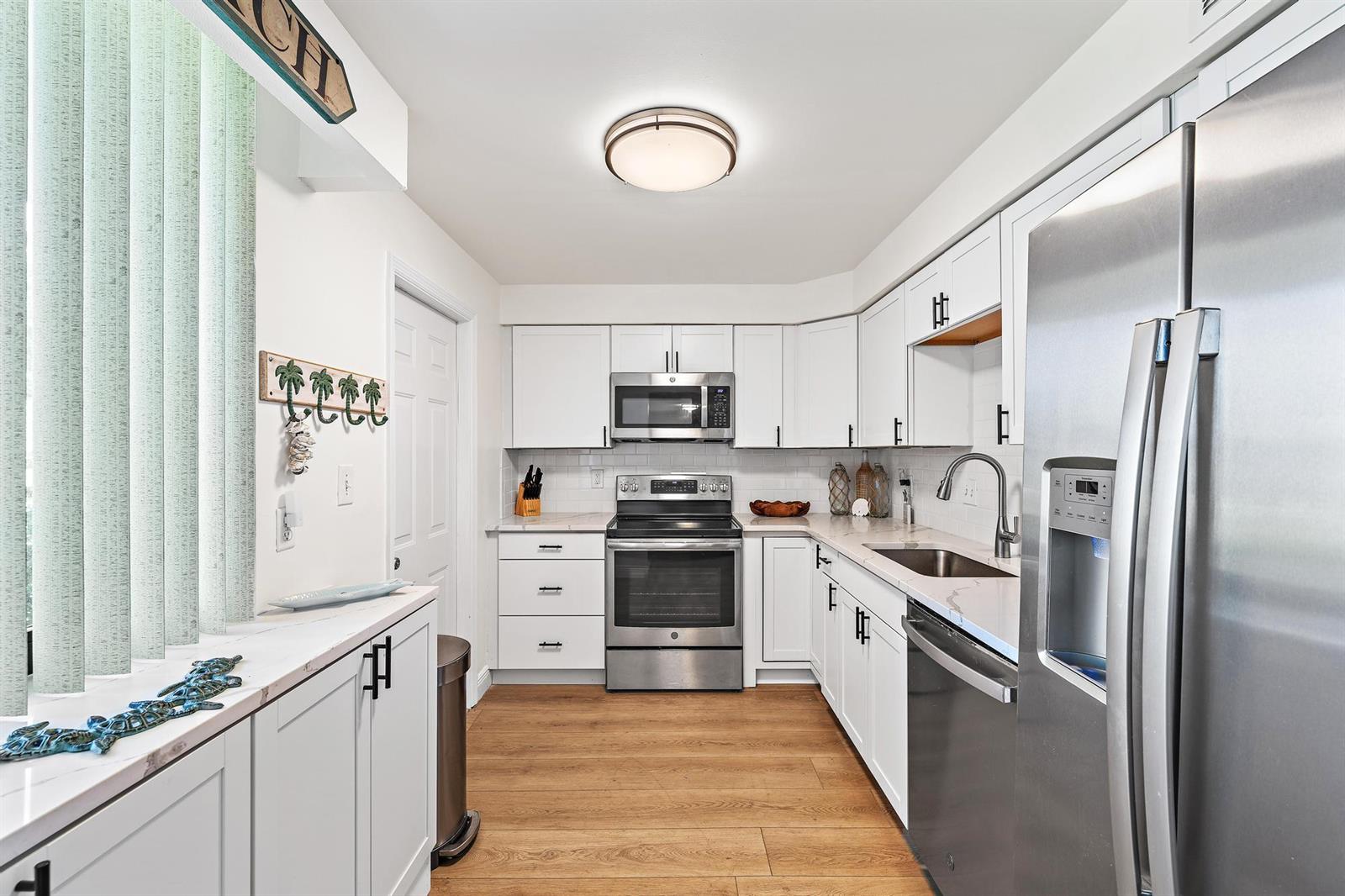 A kitchen features white cabinets, stainless steel appliances, and light wood-look flooring — 1605 S Us Highway 1 # 103, Jupiter FL 33477, JUPITER, FL