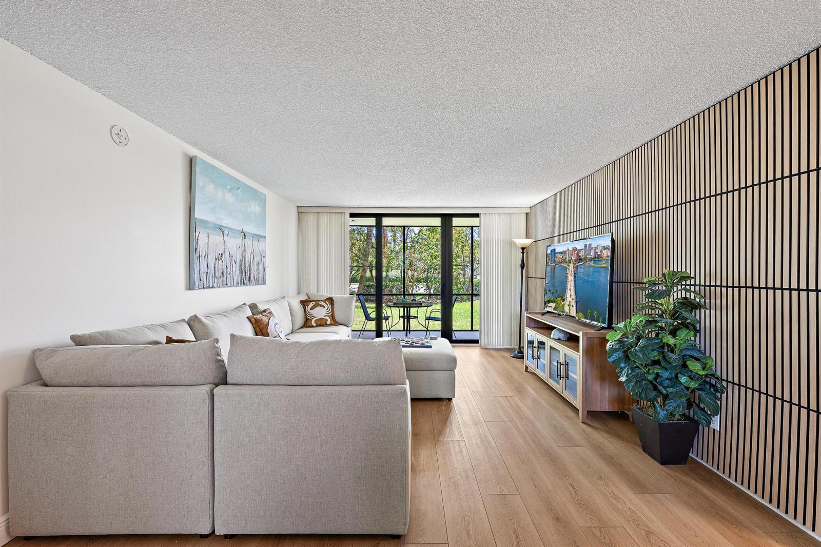 A living room features a large sectional sofa, wood flooring, and a slatted accent wall — 1605 S Us Highway 1 # 103, Jupiter FL 33477, JUPITER, FL