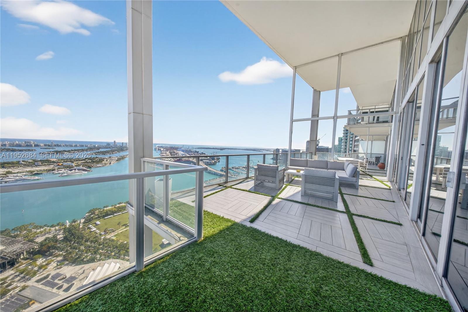 A high-rise balcony features artificial grass, tiled flooring, and outdoor seating overlooking a harbor — 1100 Biscayne Blvd # 5306, Miami FL 33132, MIAMI, FL
