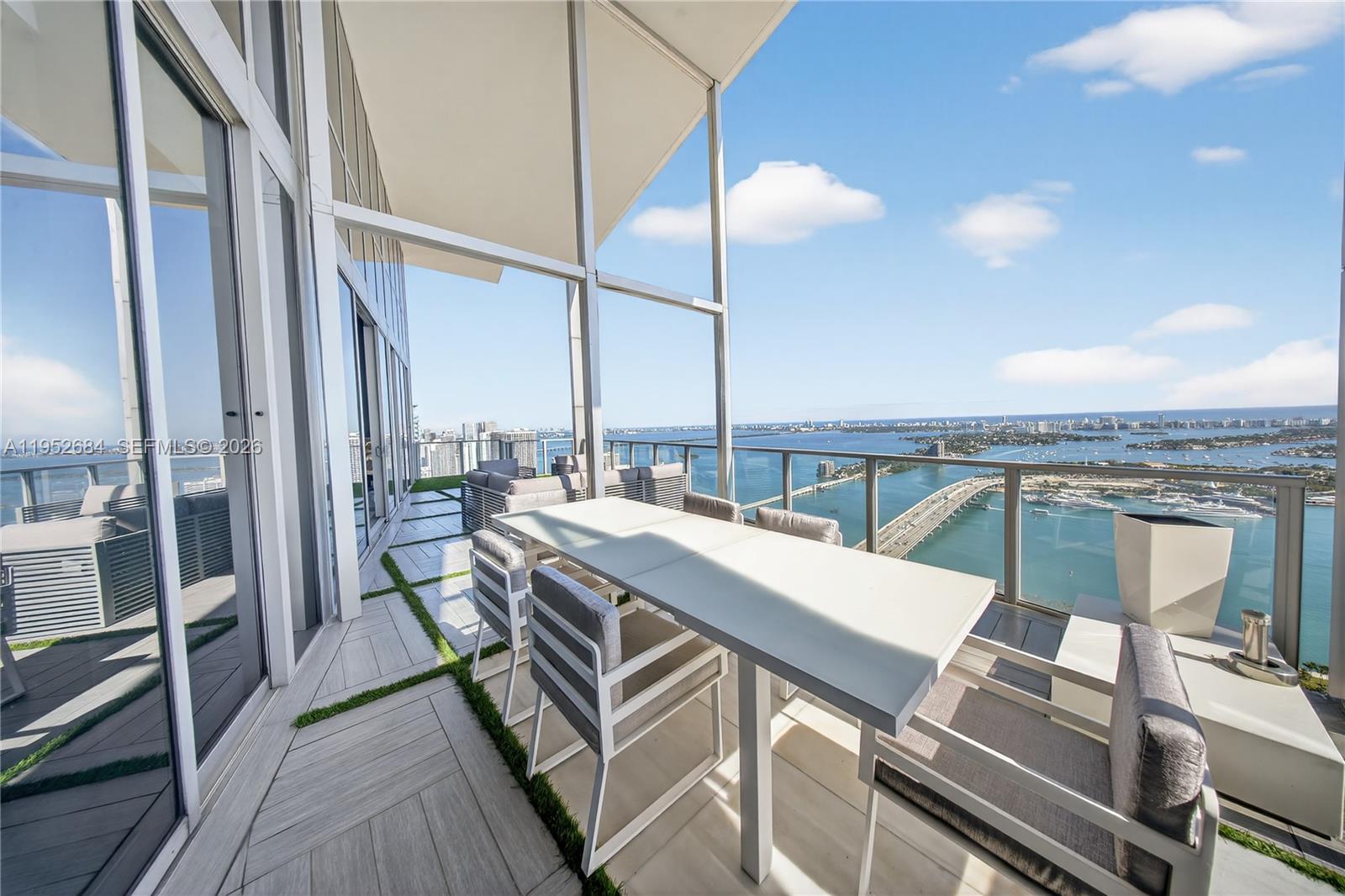 A high-rise balcony features a dining set, tiled flooring with grass accents, and water views — 1100 Biscayne Blvd # 5306, Miami FL 33132, MIAMI, FL
