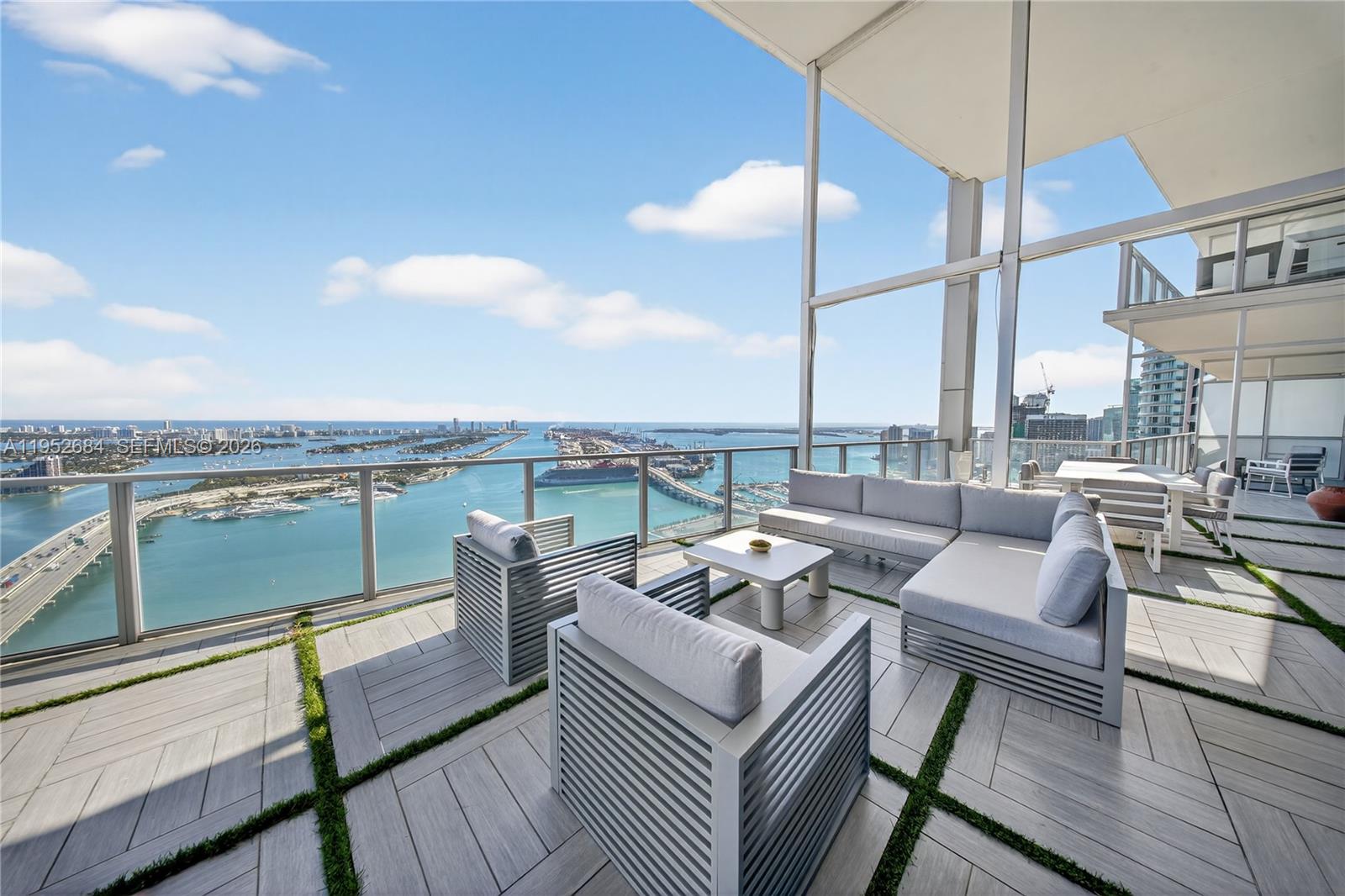 A high-rise balcony features modern outdoor furniture, tiled flooring with grass accents, and panoramic water views — 1100 Biscayne Blvd # 5306, Miami FL 33132, MIAMI, FL