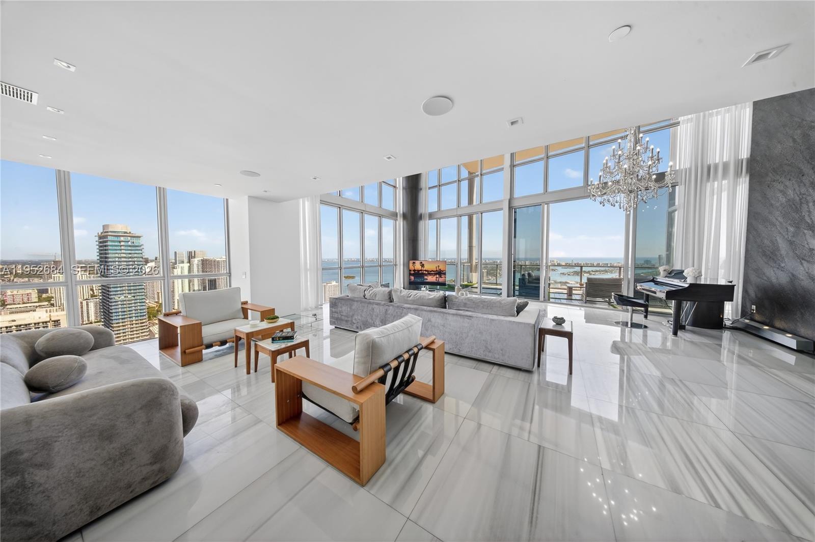 A modern living room features floor-to-ceiling windows, marble flooring, a grand piano, and city views — 1100 Biscayne Blvd # 5306, Miami FL 33132, MIAMI, FL