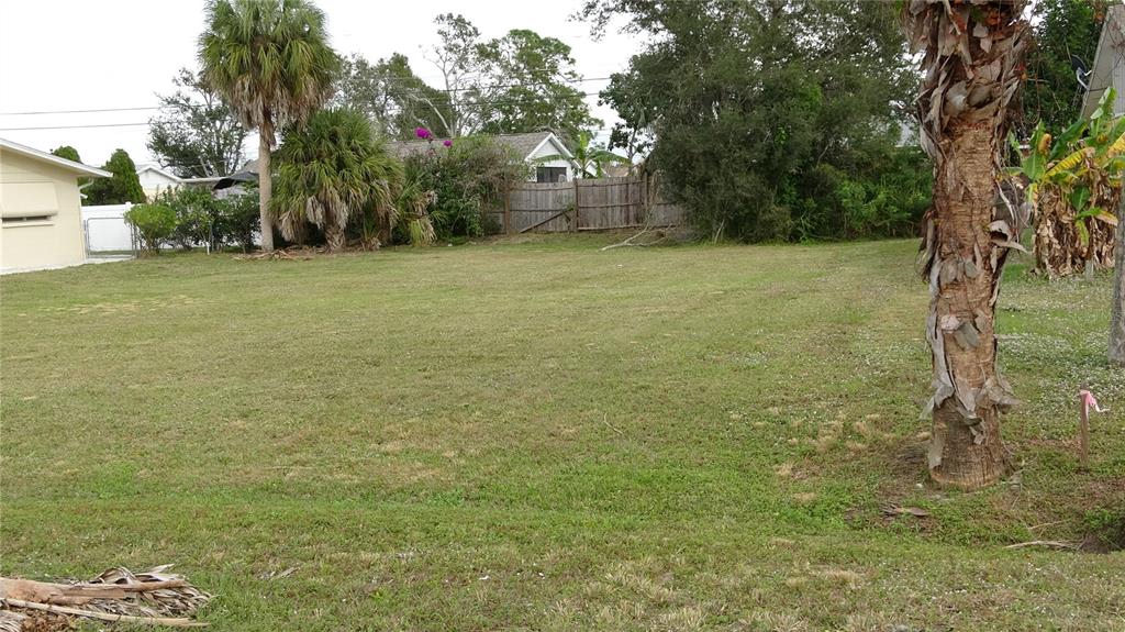 A grassy, vacant residential lot features a palm tree in the foreground and a wooden fence — GRANADA BOULEVARD, NORTH PORT, FL