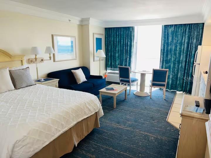 A hotel room features a bed, a blue sofa, a small table, and teal curtains — 2700 N ATLANTIC AVENUE UNIT 1206, DAYTONA BEACH, FL