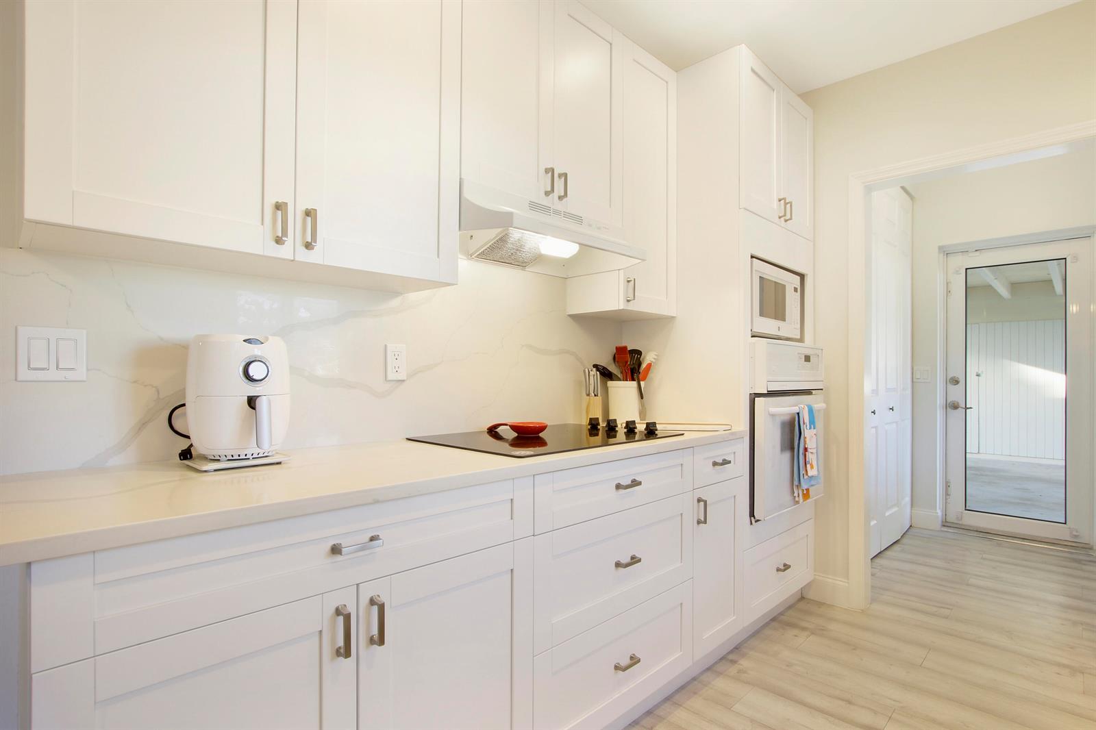 A modern white kitchen features quartz countertops, stainless steel appliances, and light wood-look flooring — 466 Tequesta Drive, Tequesta FL 33469, TEQUESTA, FL