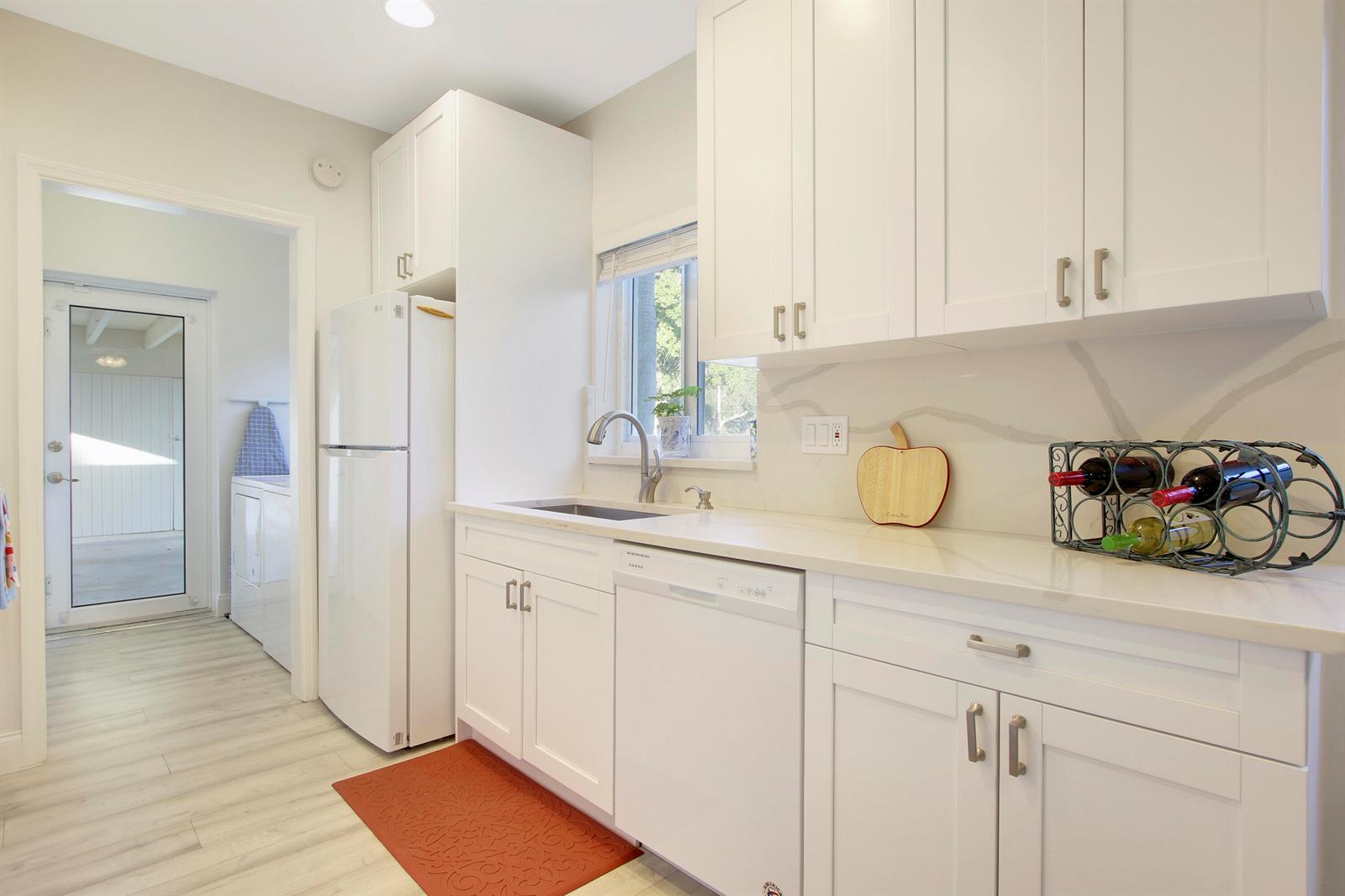 A white kitchen features shaker cabinets, quartz countertops, a dishwasher, and a wine rack — 466 Tequesta Drive, Tequesta FL 33469, TEQUESTA, FL