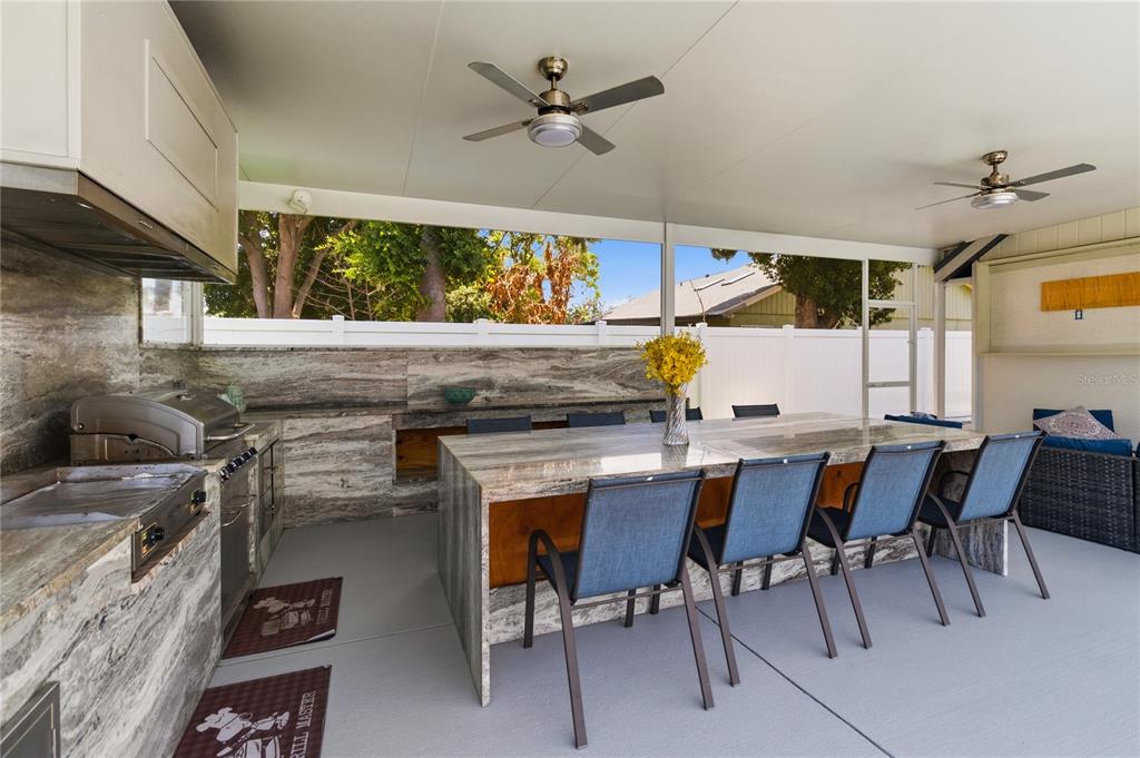 A covered outdoor kitchen and dining area features stone countertops, a grill, and seating — 8055 LESIA CIRCLE, ORLANDO, FL