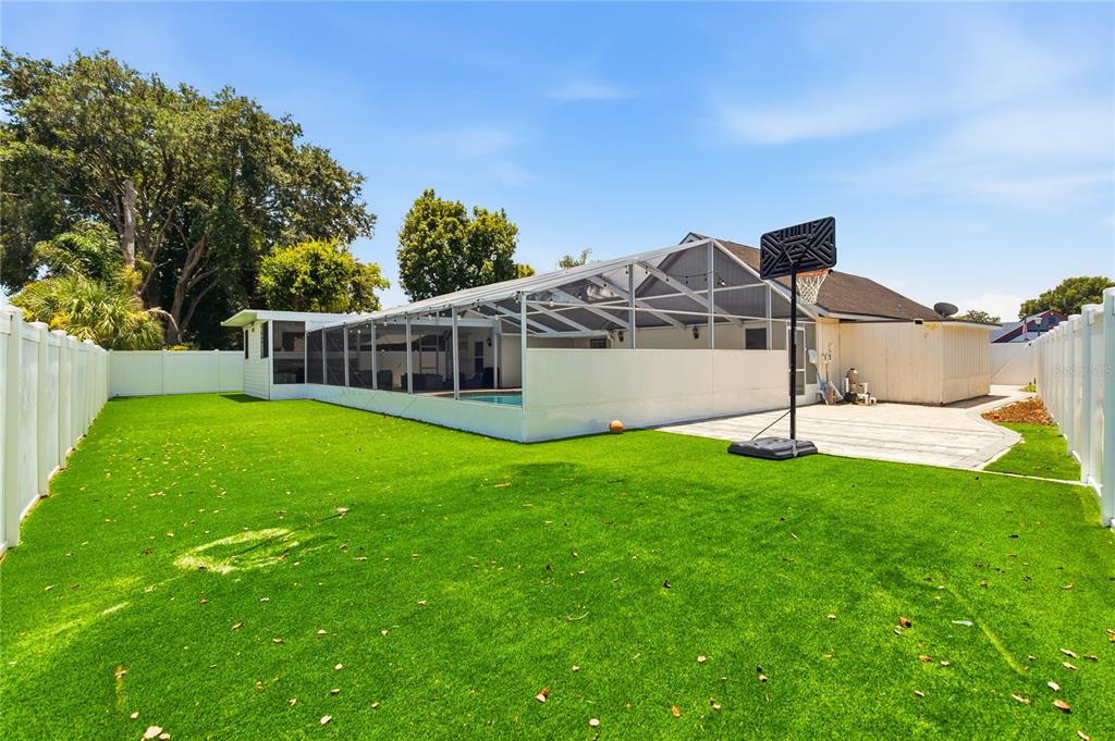 A backyard with artificial turf, a screened-in pool enclosure, and a portable basketball hoop — 8055 LESIA CIRCLE, ORLANDO, FL