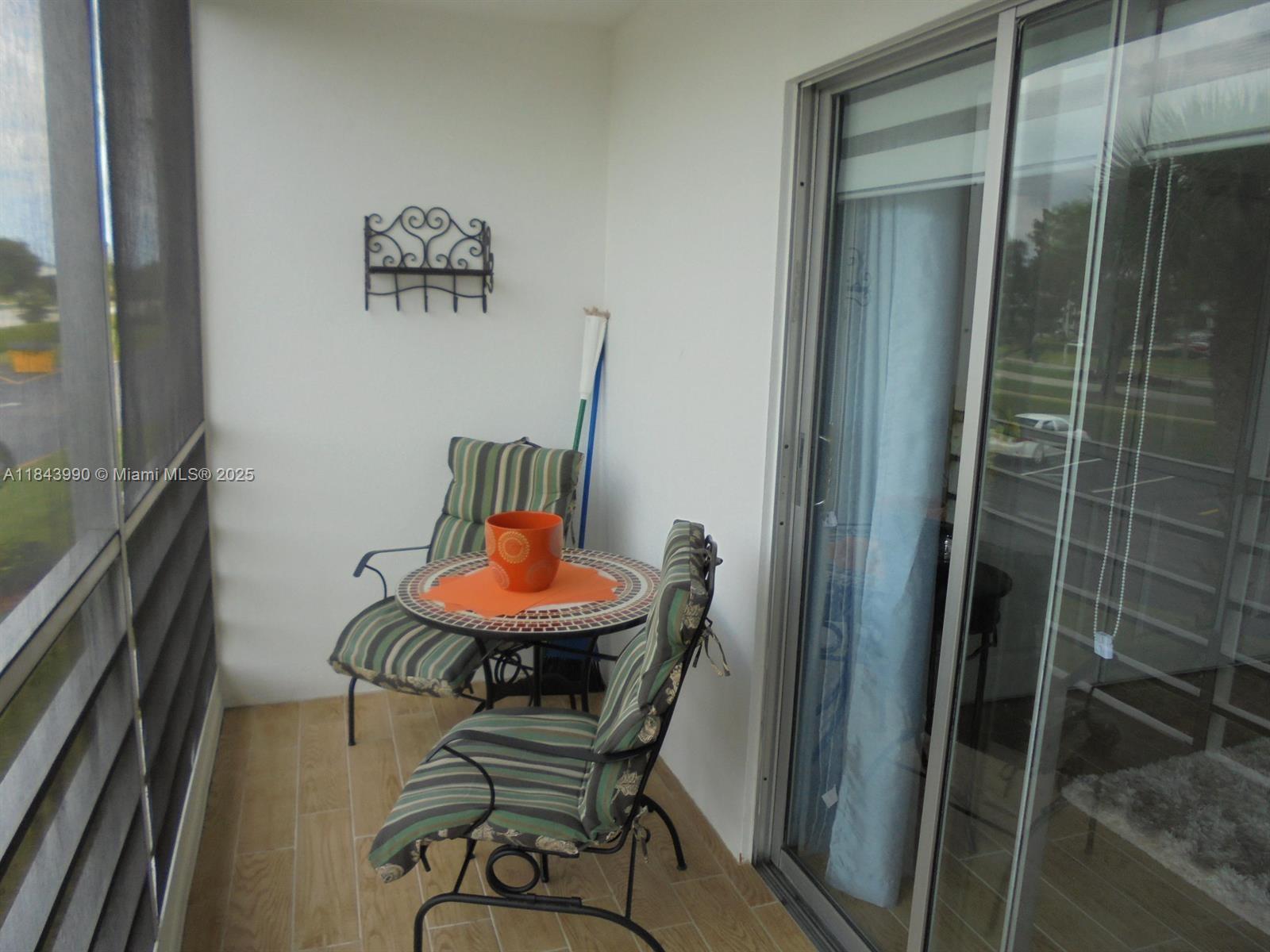 A screened-in balcony features a small bistro set, tiled flooring, and a wall-mounted rack — 400 Brighton J # 400, Boca Raton FL 33434, BOCA RATON, FL