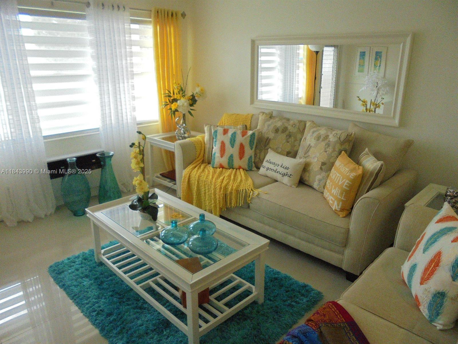 A living room features a beige sofa, a glass-topped coffee table, and bright yellow accents — 400 Brighton J # 400, Boca Raton FL 33434, BOCA RATON, FL