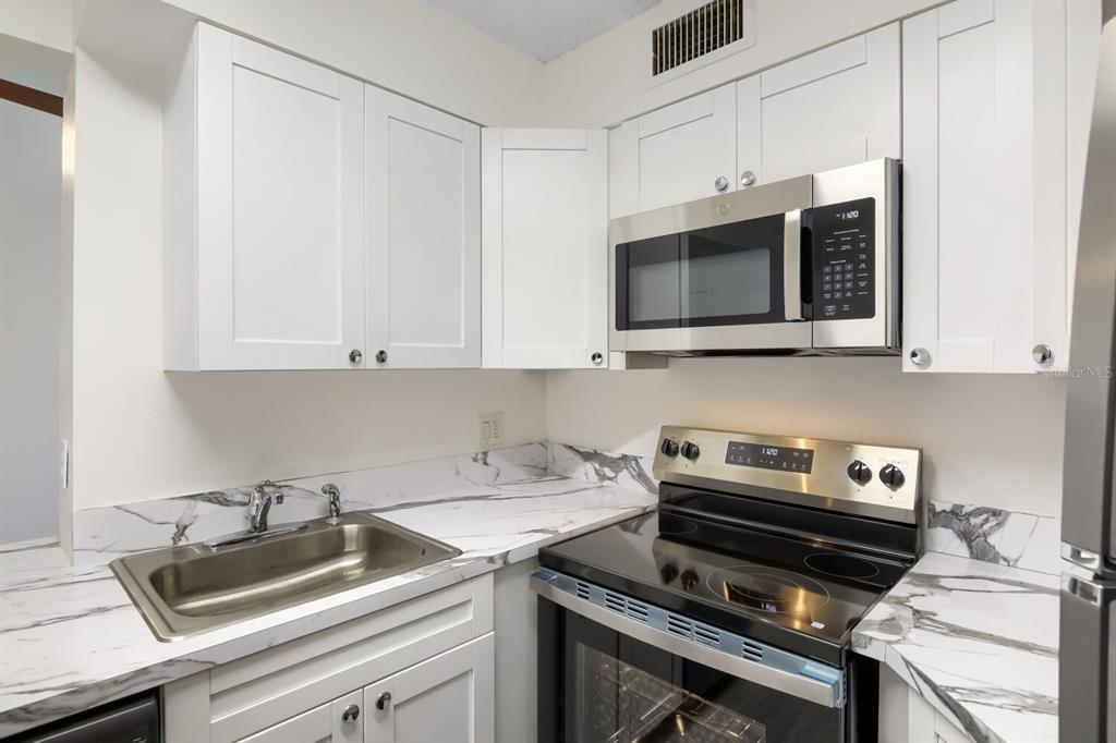 A kitchen features white cabinets, marble-patterned countertops, a stainless steel sink, and stainless steel appliances — 210 LAKE POINTE CONDO FIVE DRIVE UNIT 304, OAKLAND PARK, FL