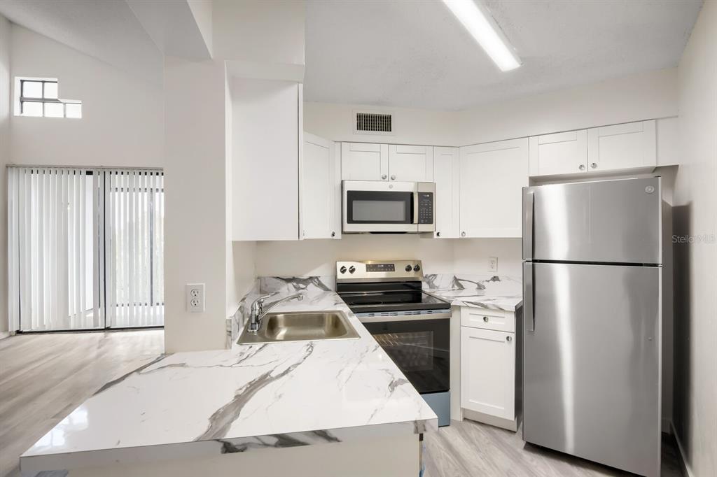 A kitchen features white cabinets, marble-patterned countertops, and stainless steel appliances — 210 LAKE POINTE CONDO FIVE DRIVE UNIT 304, OAKLAND PARK, FL