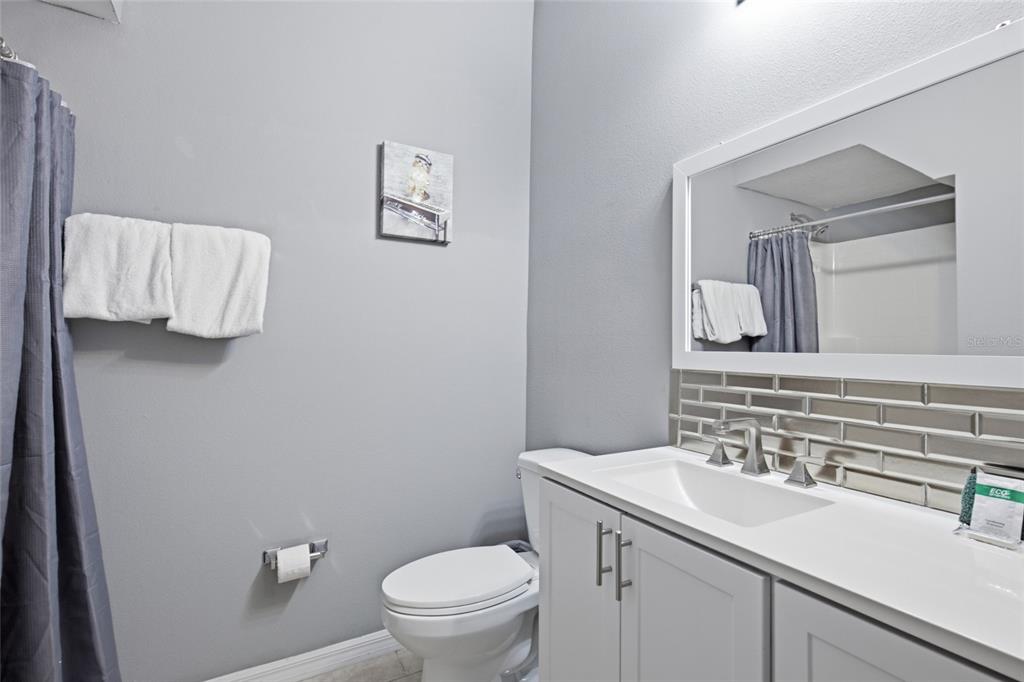 A bathroom features a white vanity, a mirror, a toilet, and a gray shower curtain — 1717 RETREAT CIRCLE, CLERMONT, FL
