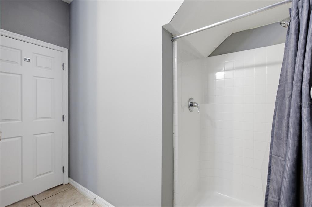 A bathroom features a white tiled shower stall next to a closed white interior door — 1717 RETREAT CIRCLE, CLERMONT, FL