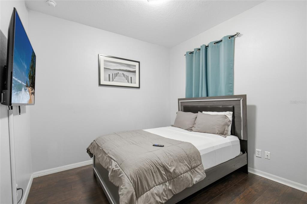 A bedroom features a bed with a grey frame, dark wood flooring, and a wall-mounted television — 1717 RETREAT CIRCLE, CLERMONT, FL
