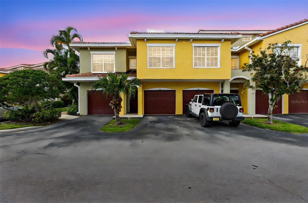 A yellow multi-unit townhouse exterior features three garage doors and a parked white Jeep — 5601 BENTGRASS DRIVE UNIT 102, SARASOTA, FL