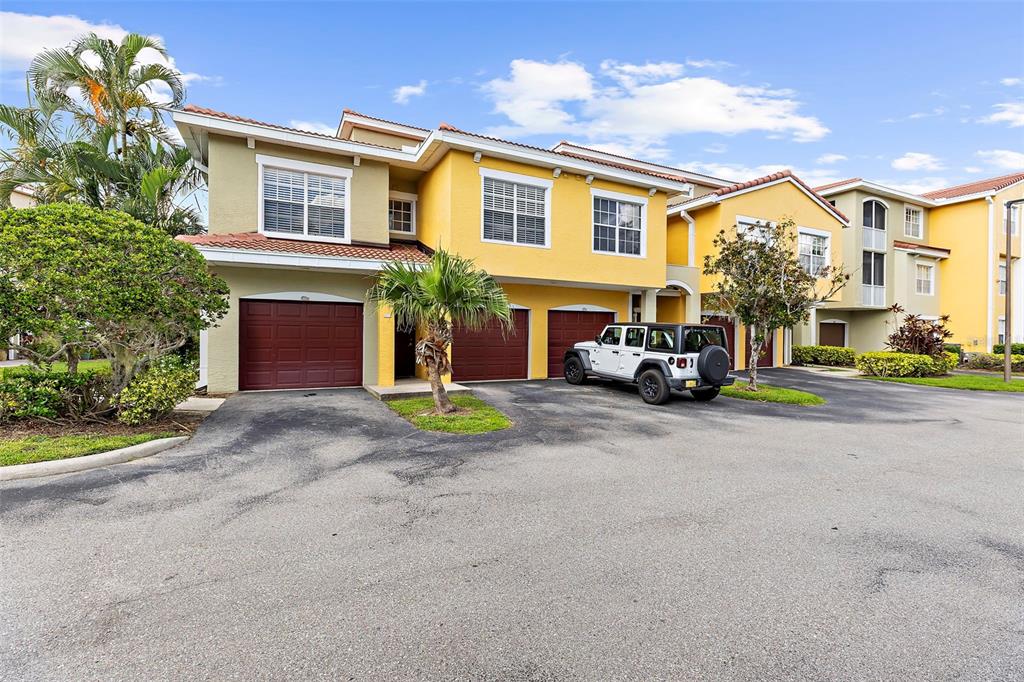 A yellow two-story townhouse with three garage doors and a white Jeep parked outside — 5601 BENTGRASS DRIVE UNIT 102, SARASOTA, FL