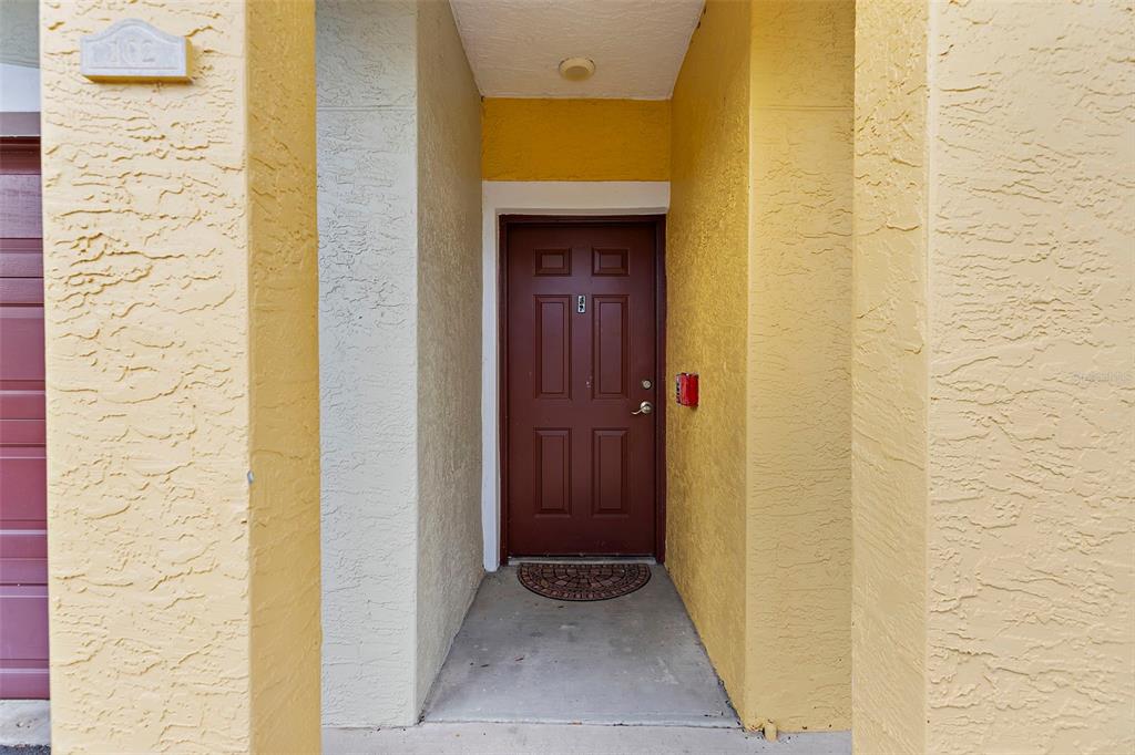 A brown front door is set within a recessed entryway with yellow stucco walls — 5601 BENTGRASS DRIVE UNIT 102, SARASOTA, FL