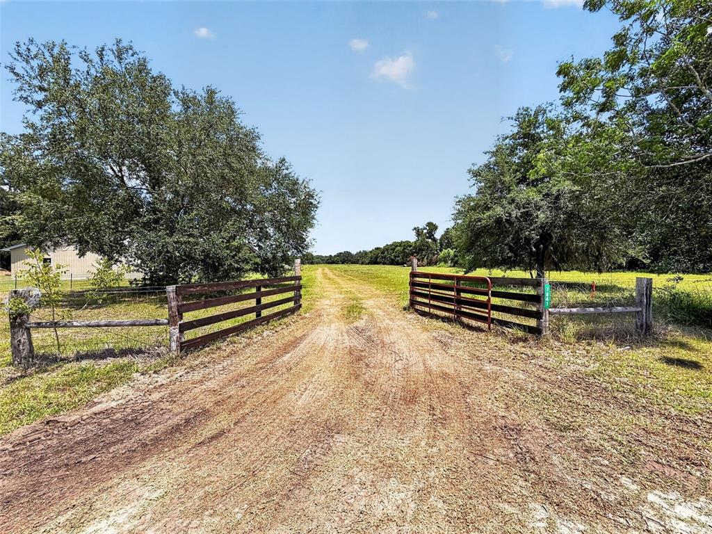 A dirt driveway leads through an open metal gate into a grassy field with trees — 7755 CR 714, CENTER HILL, FL