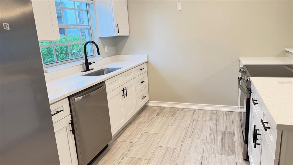 A kitchen features white cabinets, stainless steel appliances, quartz countertops, and light wood-look tile flooring — 333 ISLAND WAY UNIT 101, CLEARWATER BEACH, FL