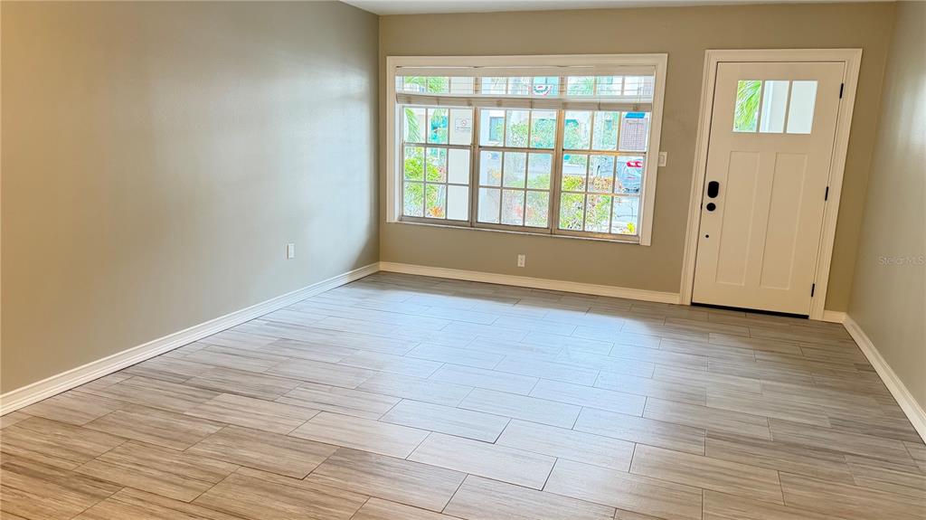 An empty room features light wood-look tile flooring, beige walls, a large window, and a door — 333 ISLAND WAY UNIT 101, CLEARWATER BEACH, FL