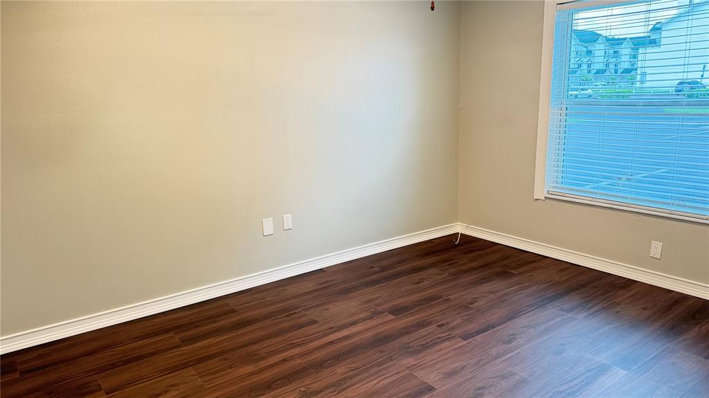 An empty room features light-colored walls, dark wood-look flooring, and a window with blinds — 333 ISLAND WAY UNIT 101, CLEARWATER BEACH, FL