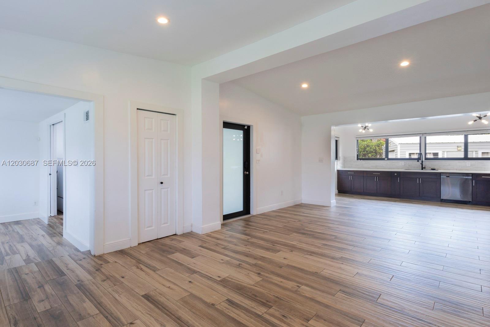 An open-concept room features wood-look tile flooring, white walls, and a view into a kitchen — 11431 SW 40th Ter, Miami FL 33165, MIAMI, FL