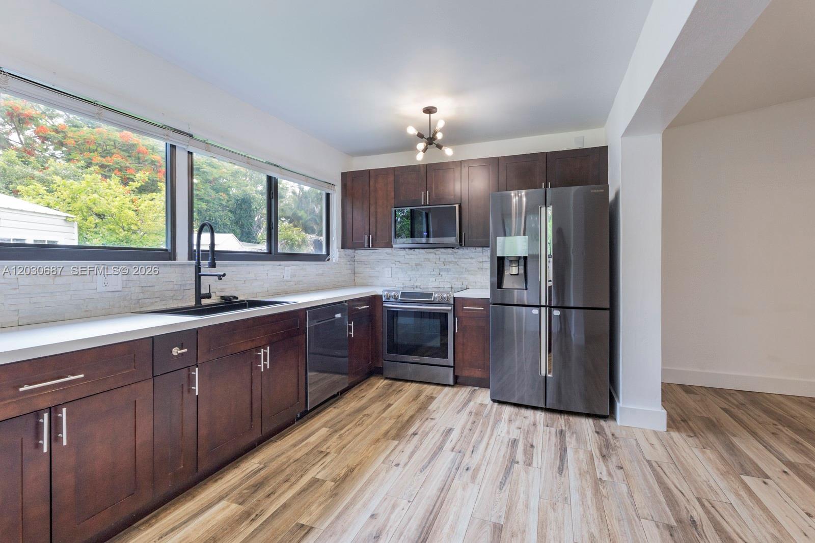 A kitchen features dark wood cabinets, stainless steel appliances, white countertops, and light wood flooring — 11431 SW 40th Ter, Miami FL 33165, MIAMI, FL