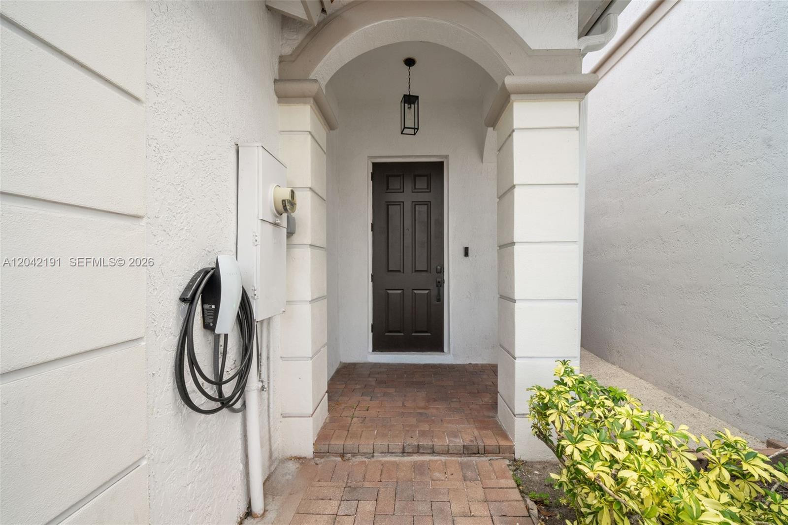 A front entryway features a dark door, brick walkway, and a wall-mounted electric vehicle charger — 10743 NW 78th Ter, Doral FL 33178, DORAL, FL