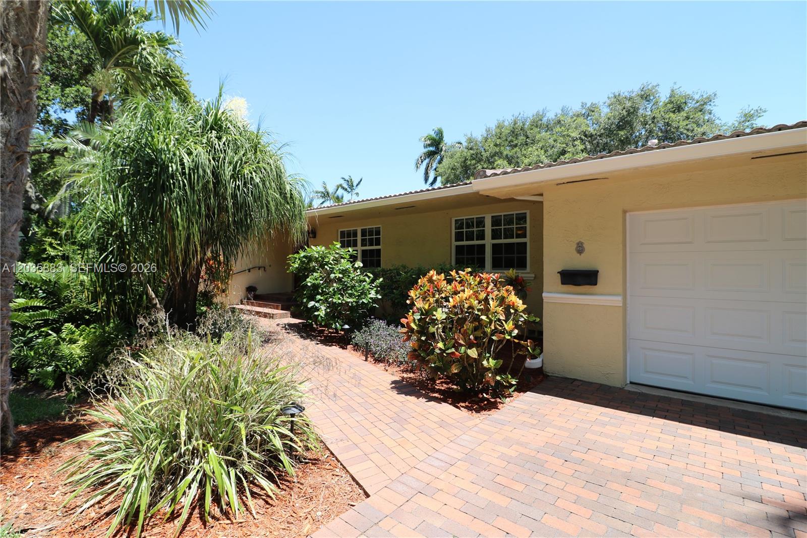 A brick walkway leads to the entrance of a yellow house with a white garage — 6160 SW 84th St, South Miami FL 33143, SOUTH MIAMI, FL