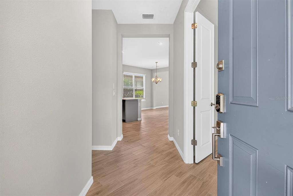 A view through an open blue front door into a hallway with wood-look tile flooring — 16443 PAYNES MILL DRIVE, BRADENTON, FL