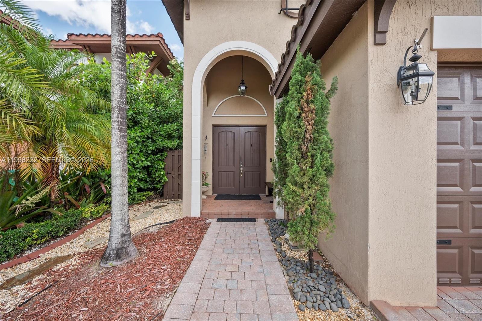 A paved walkway leads to the arched entryway of a house with double brown doors — 8755 NW 102nd Ct, Doral FL 33178, DORAL, FL