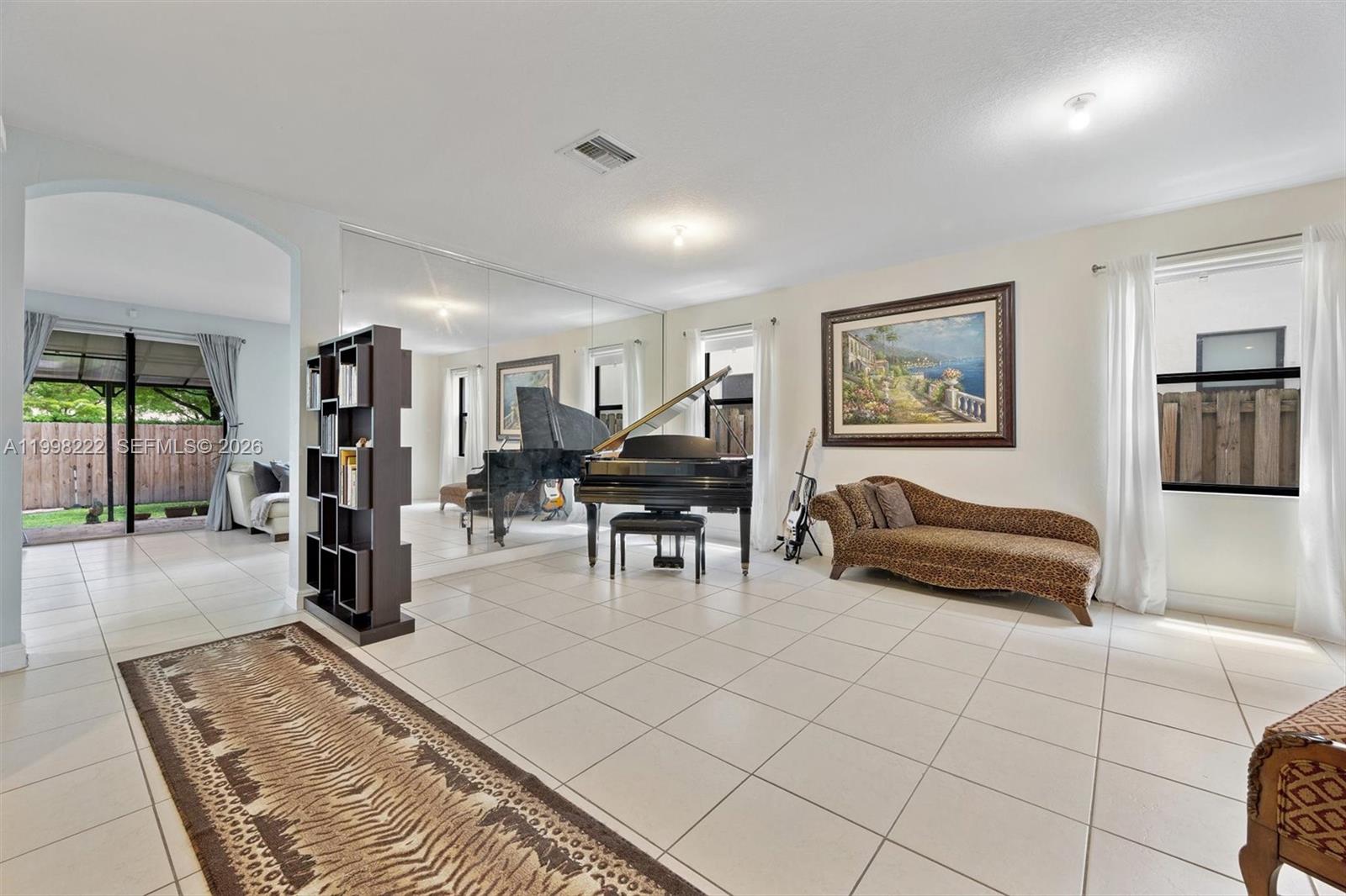 A living room features a grand piano, mirrored wall, tile flooring, and a leopard-print chaise — 8755 NW 102nd Ct, Doral FL 33178, DORAL, FL